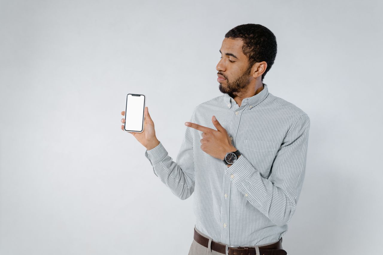 services-01 Homme confiant montrant l’écran d’un smartphone sur fond blanc, mettant en avant la technologie.